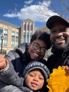 A man, woman, and child stand together in front of a church, smiling and enjoying a sunny day.